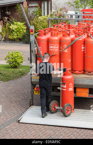 Un uomo di consegna Consegna domestici calor rosso di bombole a gas su di un carrello elevatore di coda al di fuori di una casa. Regno Unito, Gran Bretagna Foto Stock