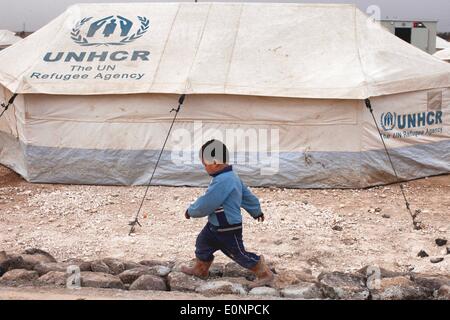 27 gennaio 2014 - Zaatari Camp, Al Mafraq Giordania - i profughi di Zaatari - un giovane ragazzo passeggiate passato un UNHCR (Alto Commissariato delle Nazioni Unite per i Rifugiati) tenda. Nei primi giorni di Zaatari tali tende dominato il paesaggio del camp. Sono lentamente essendo sostituito con strutture prefabbricate soprannominato 'Roulotte'. Nel deserto giordano, 10 chilometri dalla frontiera siriana si trova un campo profughi noto come Zaatari. Essa è la casa per oltre 110.000 sfollati fuggiti dalla guerra in Siria dal luglio 2012. La maggior parte di questi rifugiati sono dalla regione meridionale di Daraa dove la lotta ha essere Foto Stock