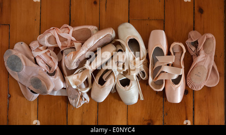 pile di vecchie scarpe da balletto usate e scarpe pointe su un pavimento in legno Foto Stock