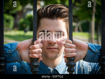 Attraente giovane uomo dietro la porta di metallo, barre di presa con le mani Foto Stock