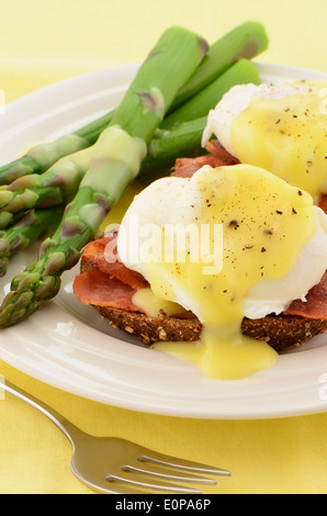 Uova alla Benedict con salsa olandese sulla ricca multigrain toast con pancetta canadese e gli asparagi Foto Stock