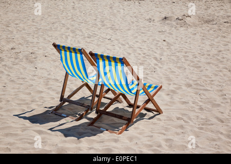 Coppia di sedie a sdraio vuote blu e gialle sulla spiaggia di Swanage, Dorset, Inghilterra, Regno Unito Foto Stock