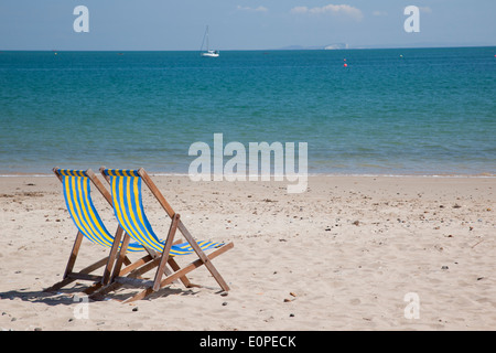 Coppia di sdraio vuote a strisce blu e gialle sulla spiaggia di Swanage, Dorset, Inghilterra, Regno Unito Foto Stock