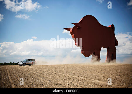 Un SUV con i giornalisti scorre attraverso un campo per visualizzare una gigantesca statua di bielorusso simbolo nazionale, il Bisonte Europeo, su una autostrada che conduce a Minsk, Bielorussia, Sabato, Maggio 10th, 2014. Le autostrade in Bielorussia non conformi con West norme europee. Western Foto Stock
