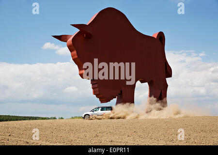 Un SUV con i giornalisti scorre attraverso un campo per visualizzare una gigantesca statua di bielorusso simbolo nazionale, il Bisonte Europeo, su una autostrada che conduce a Minsk, Bielorussia, Sabato, Maggio 10th, 2014. Le autostrade in Bielorussia non conformi con West norme europee. Western Foto Stock