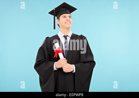 Maschio fiero studente laureato in possesso di un diploma su sfondo blu Foto Stock