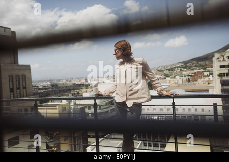 Immagine attraverso i ciechi della finestra di una giovane donna che posano su un balcone con vista della citta'. Piuttosto giovane donna in piedi sul balcone. Foto Stock