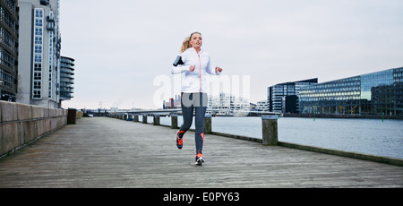 Giovane atleta femminile in esecuzione sulla passeggiata lungo il fiume. Montare la giovane donna fare jogging lungo il lungomare. Foto Stock