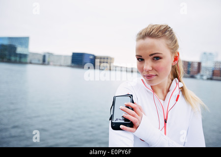 Atleta femminile della formazione all'aperto, utilizzando uno smartphone per monitorare i suoi progressi. Montare e sportività giovane atleta indossa fascia per il braccio Foto Stock