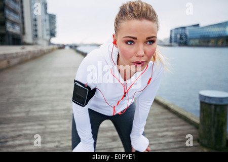 Giovane donna prendendo una pausa dall'esercizio all'esterno. Montare il giovane atleta femminile di fermarsi per riposare durante il jogging lungo il fiume. Foto Stock