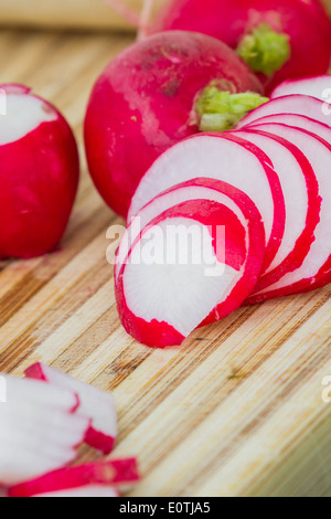 Fresche biologiche ravanelli su un tagliere, alcuni insieme e alcuni tagliati a fette Foto Stock