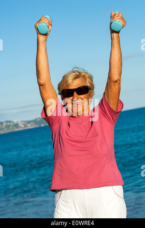 Senior donna facendo esercizio muscolare sulla spiaggia. Foto Stock