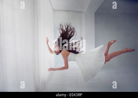 Una donna floating orizzontalmente in una camera vicino alla finestra Foto Stock