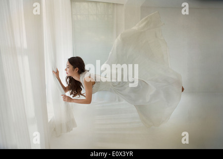 Una donna floating orizzontalmente in una camera vicino alla finestra Foto Stock