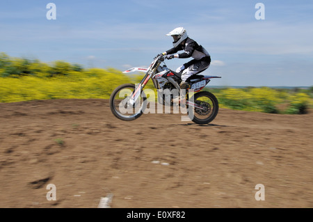 Il Motocross è una forma di moto racing tenutasi il ruvido racchiuso off-road circuiti. Moto rider su scramble bike, equitazione attraverso il campo Foto Stock