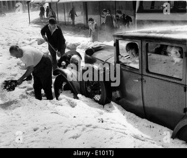 Maltempo - due uomini pala neve dalla parte anteriore della vecchia auto bloccata in deep snow drift su strada come i bambini guardano da Windows. Foto Stock