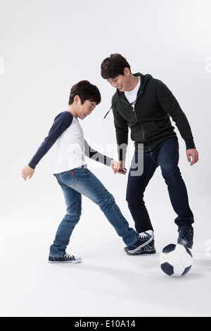 Un padre e un figlio a giocare con un pallone da calcio Foto Stock