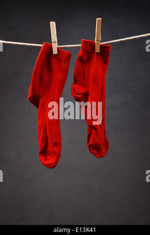 Vecchio calzini rossi appeso sulla corda attaccata con clothespins a secco. Foto Stock