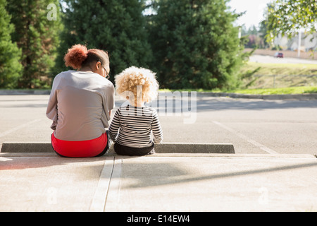 Razza mista sorelle seduti all'aperto Foto Stock