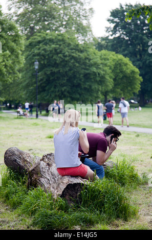 Paio utilizzando i telefoni cellulari in Park - London REGNO UNITO Foto Stock