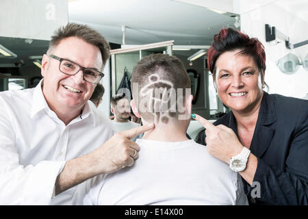 Due parrucchieri Gerhard Ostler e Sylvia Ostler in posa con un cliente che ha ricevuto una Coppa del Mondo di Calcio capelli tatuaggio Foto Stock