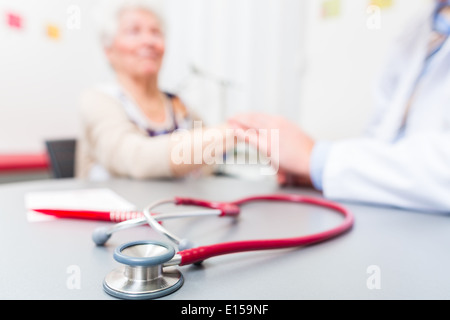 Medico seduto con il titolare di pensione o di rendita in chirurgia consultazione ora a scrivania Foto Stock