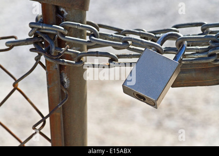 Primo piano di una chiave di metallo di blocco e blocco catena di una rete metallica recinzione mantenendo la gente fuori e in Foto Stock