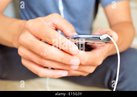 Primo piano di un giovane uomo che ascolta musica o parlando con un auricolare in uno smartphone Foto Stock