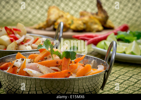 Indian il pollo su un piatto di portata con ciotole di insalata e una decorazione di calce, corriander e peperoncino Foto Stock