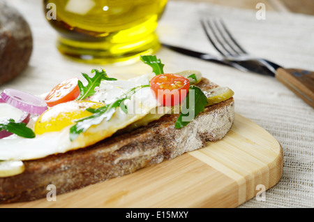 Uovo fritto e verdi di sandwich aperto sul bordo di taglio Foto Stock