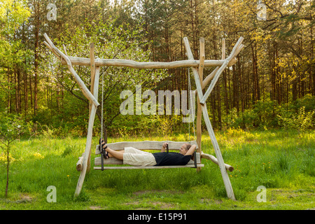 Uomo adulto di lettura di un ebook perché giacente su un altalena Foto Stock