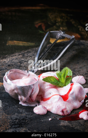 Fusione di gelato alla fragola con menta fresca e cucchiaio di metallo sulla tavola nera. Foto Stock