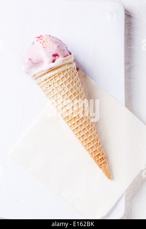 Cono in cialda con gelato alla fragola bianca sul bordo di taglio. Foto Stock