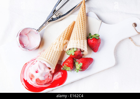 Coni con gelato alla fragola con lo sciroppo di menta e fragole fresche servita su bianco tagliere su bianco tessile. Foto Stock