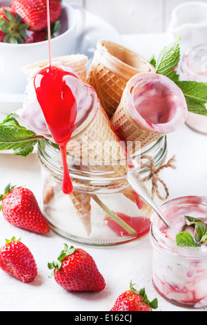 Coni con gelato alla fragola con la colata e sciroppo di fragole fresche servita in un barattolo di vetro su bianco tessile. Foto Stock