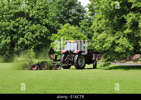 Trattore tirando una macchina falciatrice su un Villaggio Verde Foto Stock