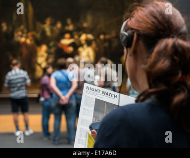 Donna ascoltare un audio guida e la lettura su di Rembrandt La ronda di notte nel Rijksmuseum Amsterdam, Paesi Bassi Foto Stock