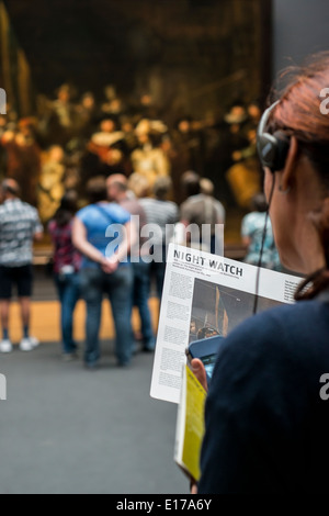 Donna ascoltare un audio guida e la lettura su di Rembrandt La ronda di notte nel Rijksmuseum Amsterdam, Paesi Bassi Foto Stock