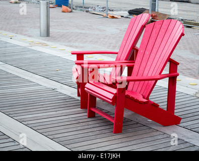 Due rossi sedie Adirondack alla base dell'onda coperta di Queens Quay a Toronto. Foto Stock