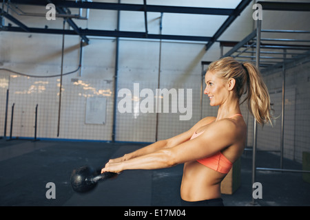 Vista laterale di felice giovane donna esercita con bollitore bell in palestra. Caucasian atleta femminile facendo crossfit allenamento in palestra. Foto Stock