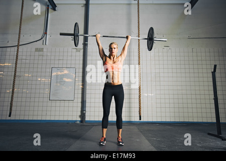 Lunghezza completa immagine di forte donna giovane con barbell e piastre di peso di overhead crossfit facendo esercizio. Montare atleta femminile. Foto Stock