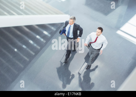 Uomini d'affari con le valigie in esecuzione nella lobby Foto Stock