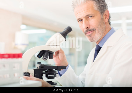 Ritratto di fiducioso scienziato usando microscopio in laboratorio Foto Stock