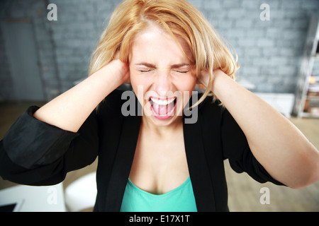 Urlando giovane donna con orecchi chiusi in ufficio Foto Stock
