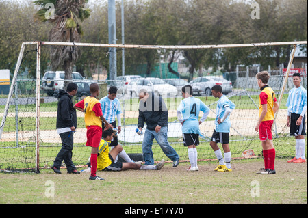 Feriti junior portiere di calcio ricevono il trattamento, i giocatori a guardare, Cape Town, Sud Africa Foto Stock