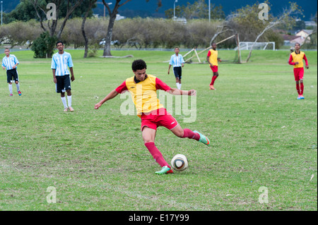 Junior giocatore di football calciare il pallone, altri giocatori a guardare, Cape Town, Sud Africa Foto Stock