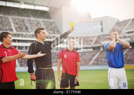 Arbitro giallo lampeggiante carta al giocatore di calcio sul campo