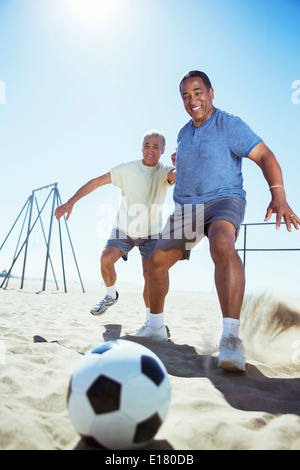 Alti uomini giocano a calcio sulla spiaggia Foto Stock