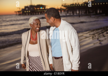 Coppia senior camminando sulla spiaggia al tramonto Foto Stock