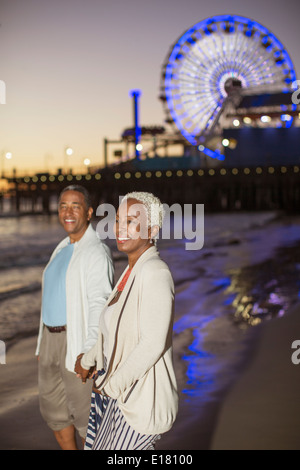 Coppia senior camminando sulla spiaggia al tramonto Foto Stock